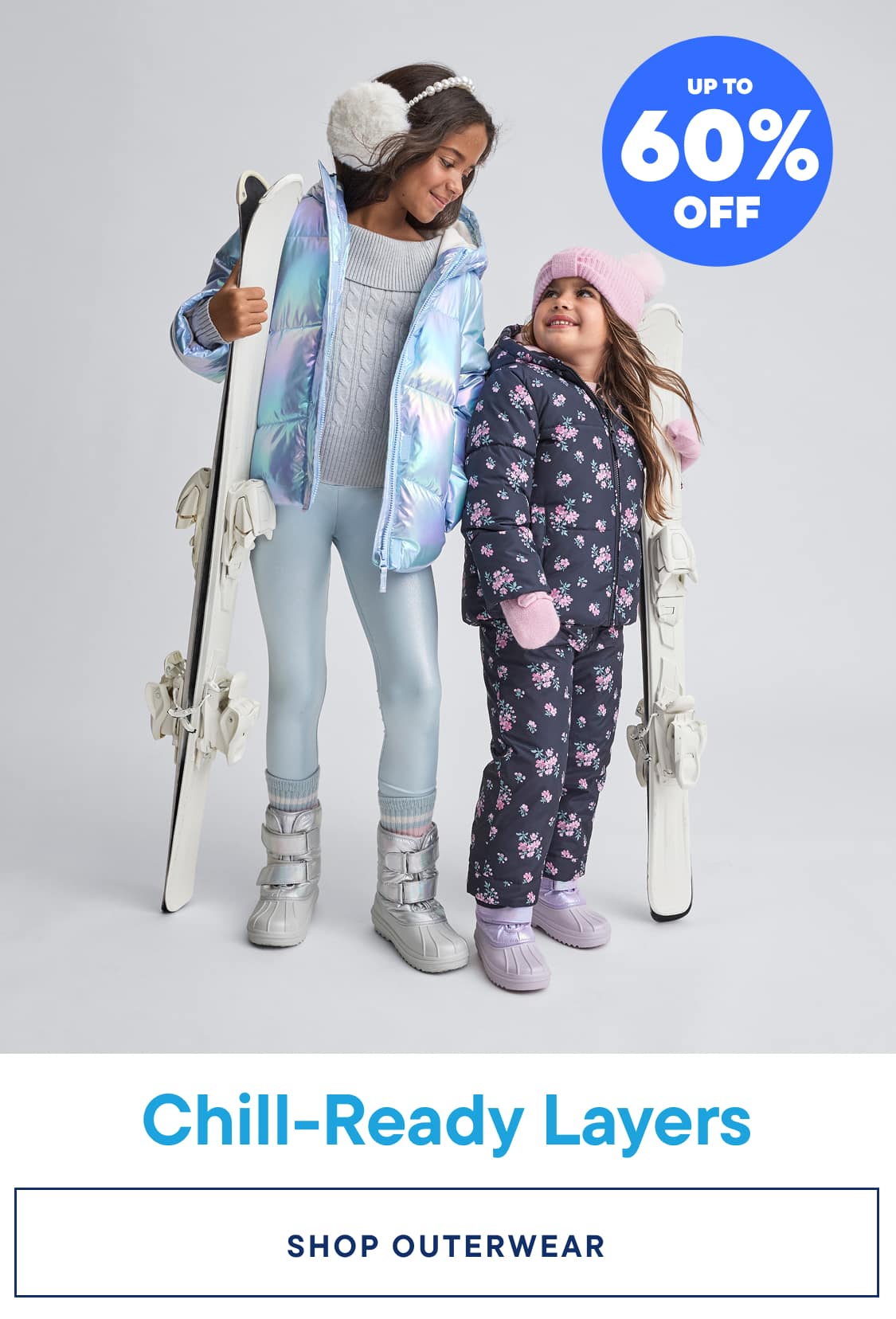 Two young girls wearing colorful winter outfits, including puffy jackets and snow pants, standing in front of a plain background with a promotional banner advertising "Chill-Ready Layers" and "Up to 70% Off" on graphic tees.