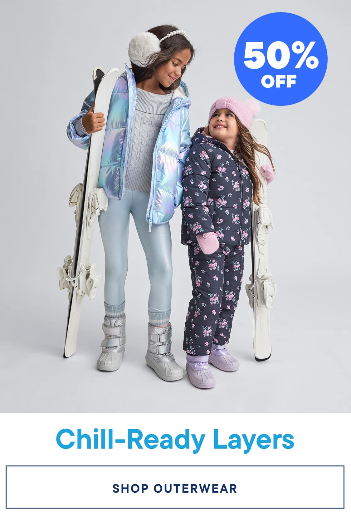 Two young girls wearing colorful winter outfits, including puffy jackets and snow pants, standing in front of a plain background with a promotional banner advertising "Chill-Ready Layers" and "Up to 50% Off" on graphic tees.