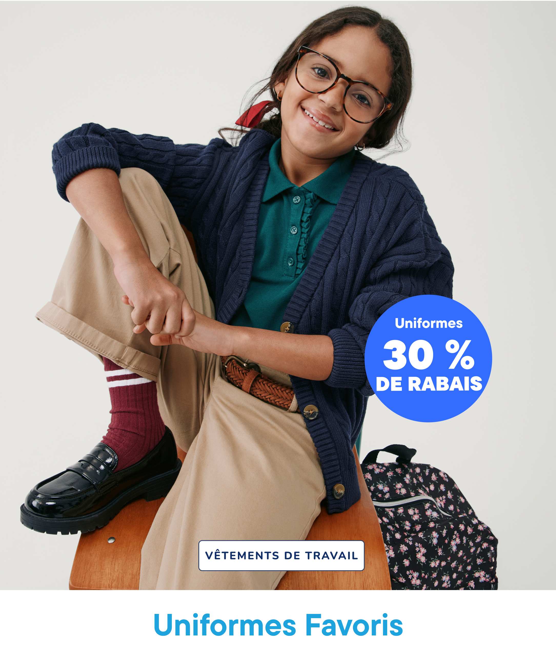 A smiling young woman wearing glasses and a navy blue sweater sits on a wooden stool, with a 30% off uniform sale sign in the background.