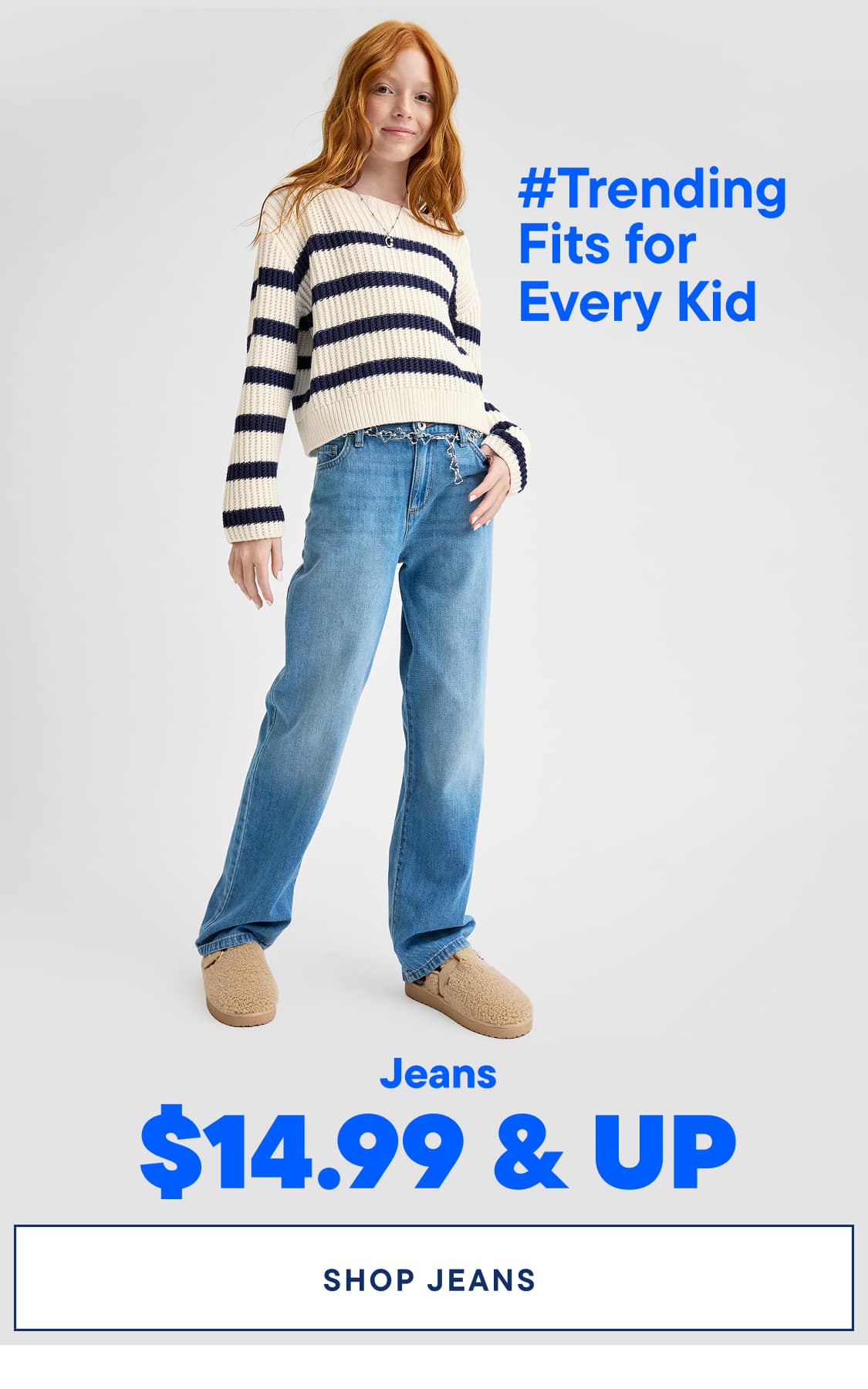 A young woman with long, red hair is wearing a striped sweater and light-colored jeans, standing against a plain white background with a price tag for jeans displayed.