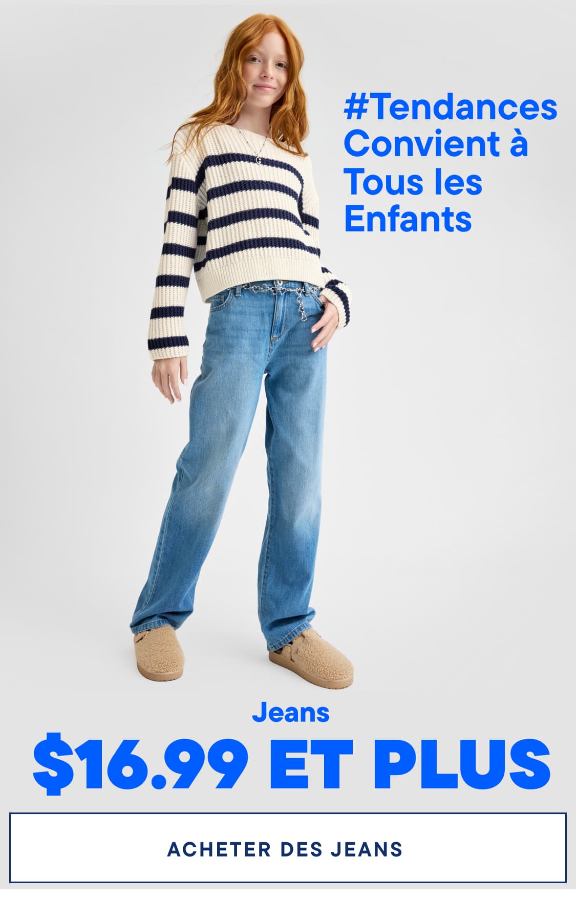 Une jeune femme aux longs cheveux roux se tient debout, vêtue d'une tenue décontractée composée d'un pull rayé et d'un jean clair, l'étiquette de prix du jean étant bien visible au premier plan.