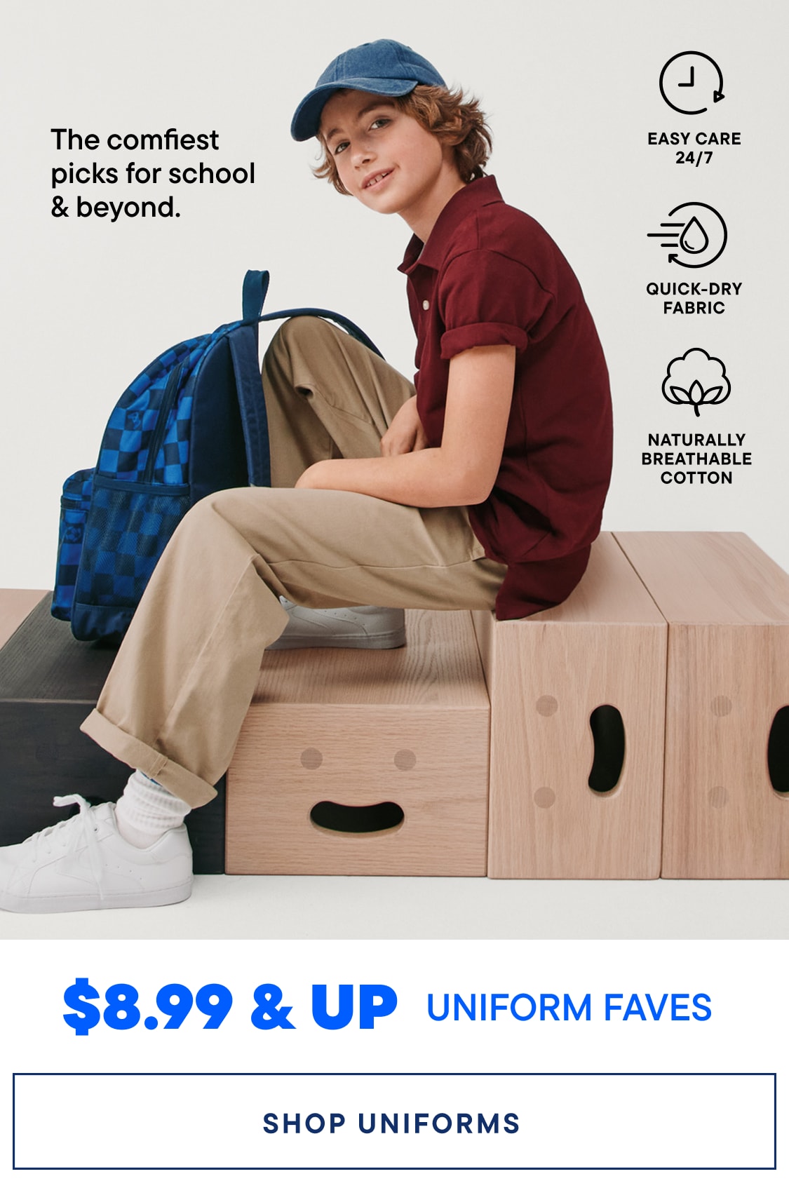 A smiling young woman wearing glasses, a navy blue cardigan, and a green shirt sits on a wooden bench, with a sign advertising uniform prices in the background.