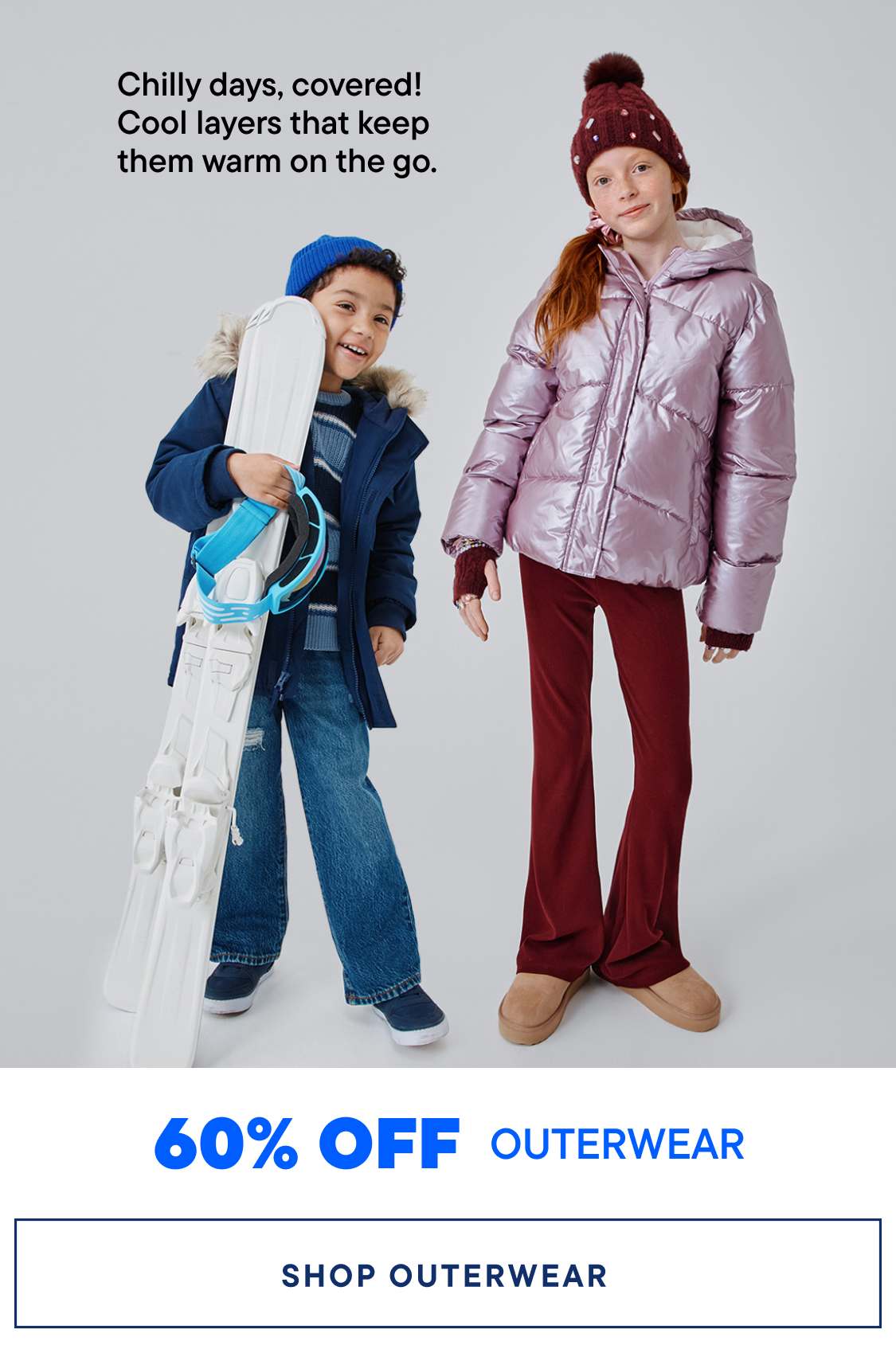 Two young children, a boy and a girl, are wearing warm winter outerwear and smiling at the camera. The background is a plain white backdrop, highlighting the focus on the children's colorful and cozy clothing.