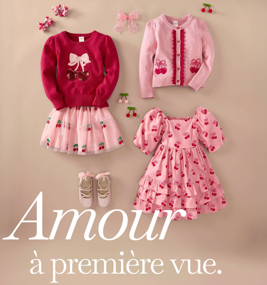 Une collection d'adorables vêtements pour enfants roses et rouges, comprenant un pull à nœud, un cardigan à motifs de cerises, une jupe en tulle et une robe à motifs, le tout disposé sur un fond clair avec le texte « Coup de foudre ».