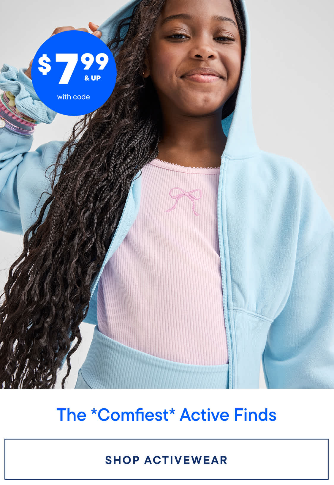 A young woman with long, curly hair wearing a pink top and a light blue jacket, smiling at the camera against a blue background with a price tag overlay.
