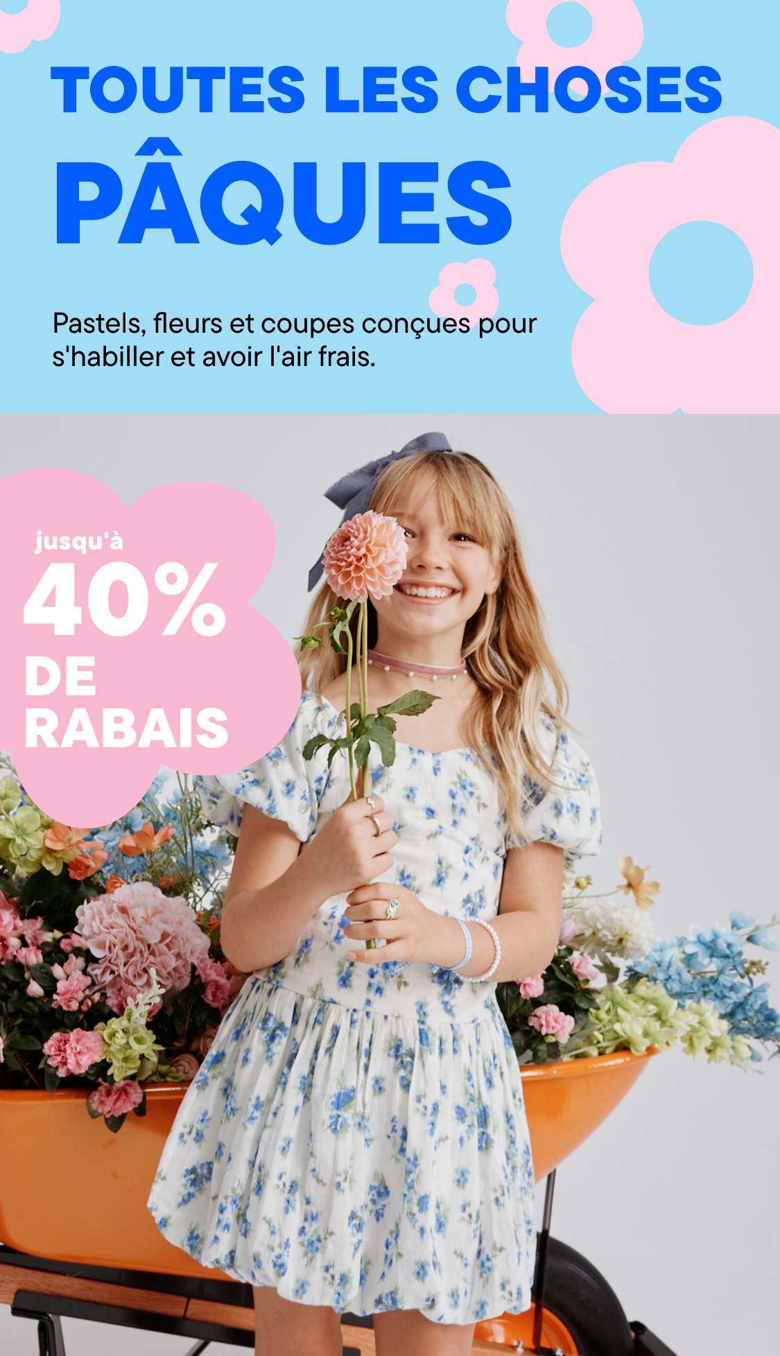 Une jeune femme aux cheveux blonds bouclés sourit et tient un bouquet de fleurs devant un fond floral coloré.