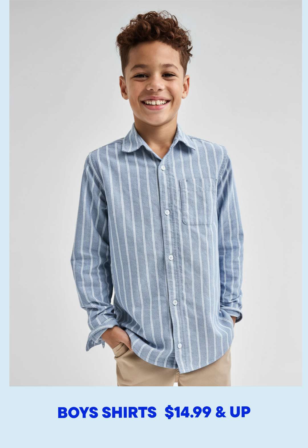 A young boy with curly hair is smiling while wearing a striped button-up shirt against a plain white background.