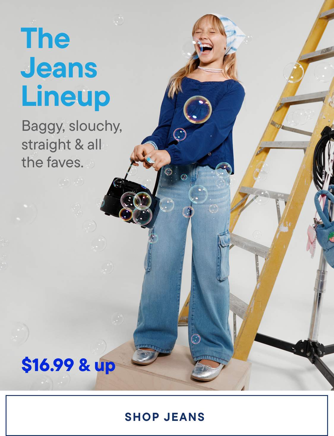 A woman wearing a blue sweater and jeans stands in front of a ladder, surrounded by various accessories and props, with the text "The Jeans Lineup" prominently displayed.