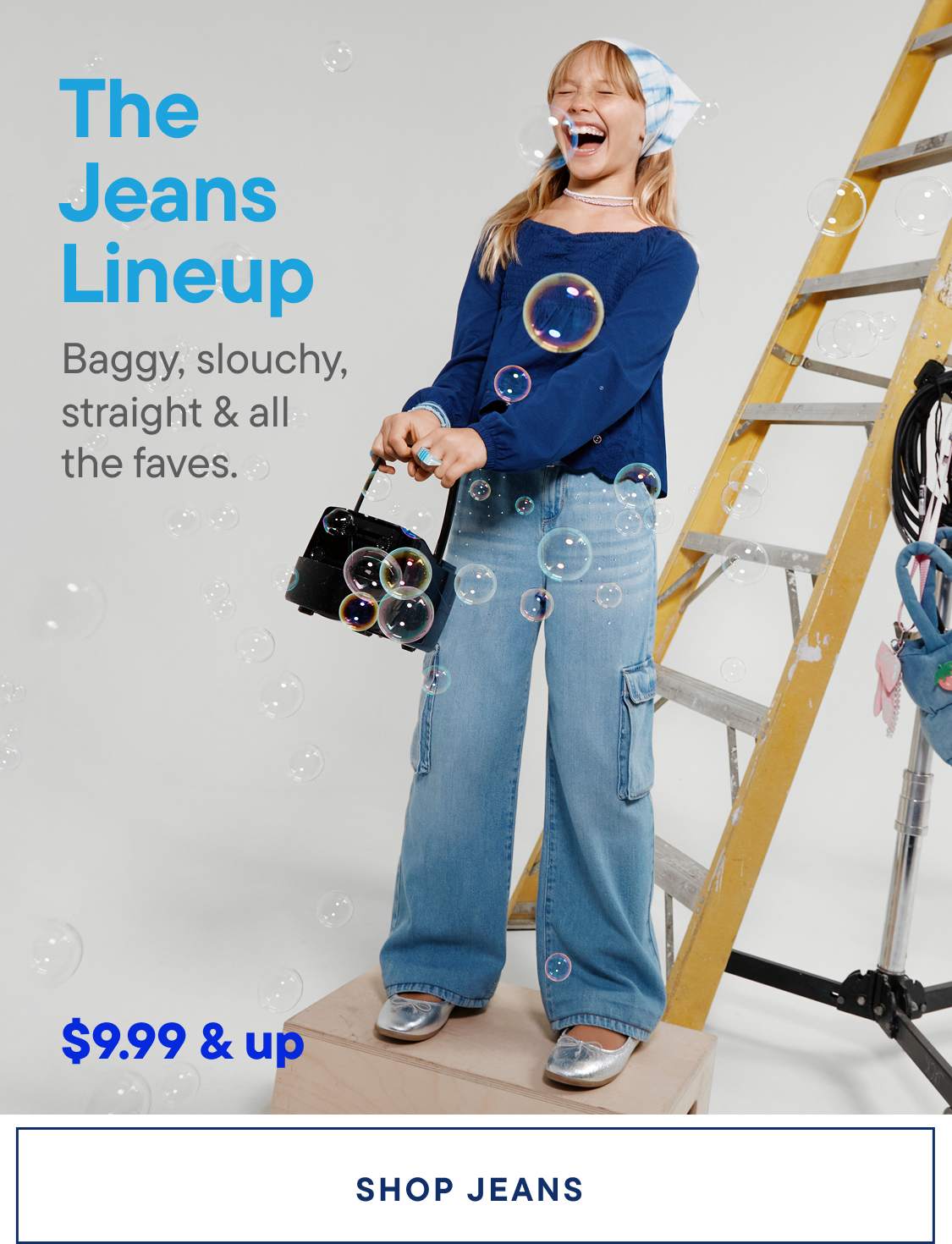 A woman wearing a blue sweater and jeans stands in front of a ladder, surrounded by various accessories and props, with the text "The Jeans Lineup" prominently displayed.