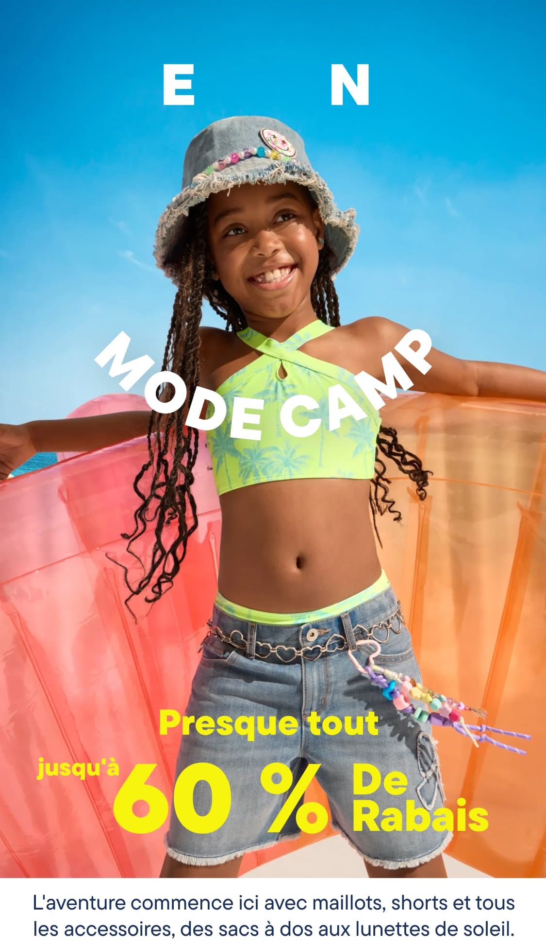 Une jeune fille souriante en maillot de bain et chapeau tient un grand radeau gonflable sur une plage ensoleillée, avec l'océan et une foule en arrière-plan.