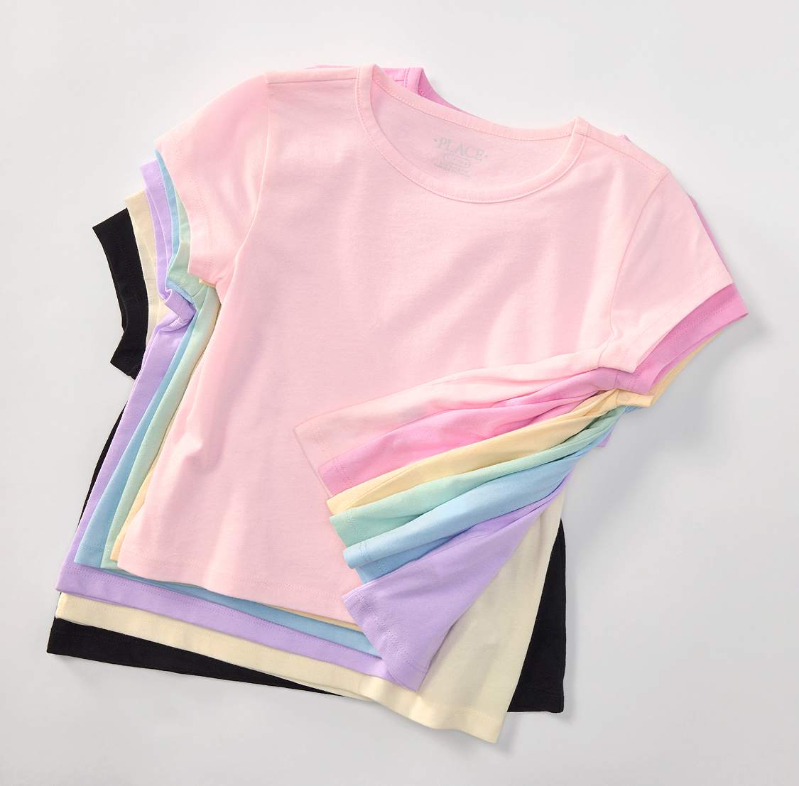A stack of pastel-colored t-shirts, ranging from black to light pink, are neatly arranged on a white background.