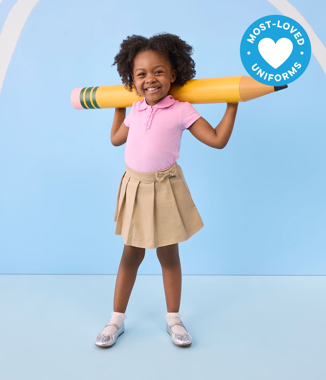 A smiling young girl in a pink polo shirt and khaki skirt holds a giant yellow pencil over her shoulders against a light blue background with white stripes.