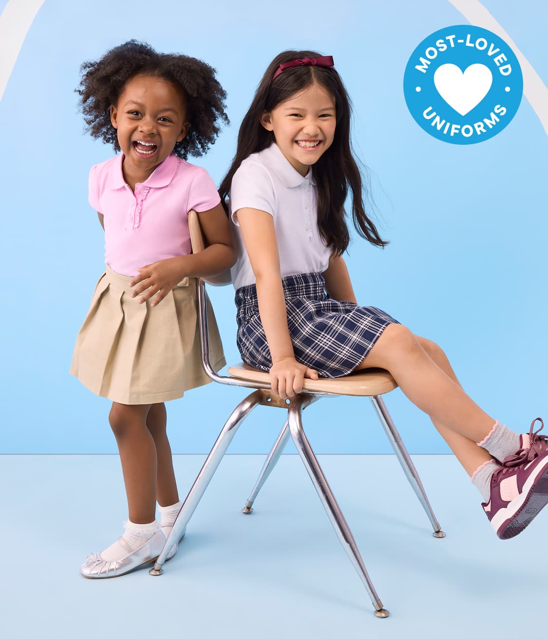 Two young girls in school uniforms smile in front of a light blue background with a Most-Loved Uniforms badge.