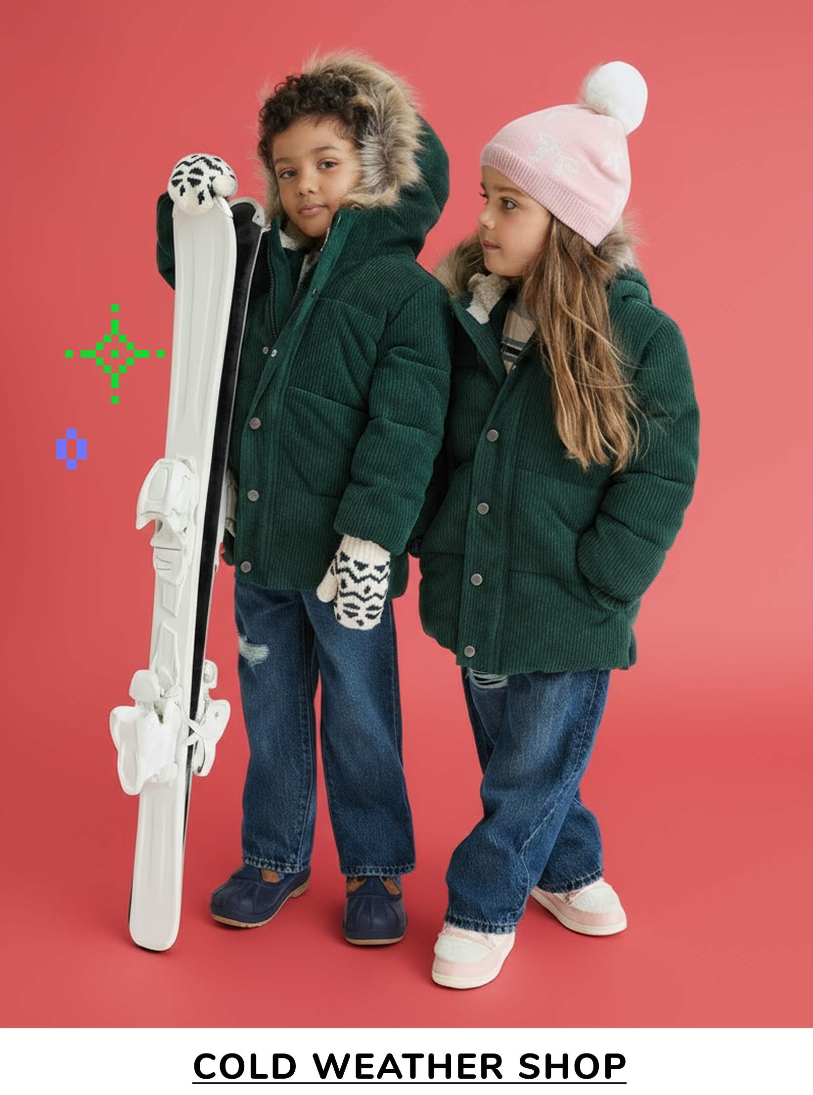 Two young children, a boy and a girl, are standing together in front of a red background. They are both wearing warm winter coats and holding ski equipment, suggesting they are preparing for cold weather activities.