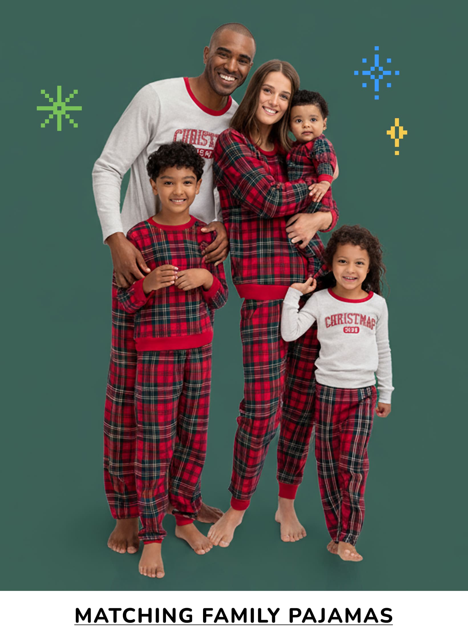 A family of four, dressed in matching red and black plaid pajamas, stands together in front of a green background with festive holiday decorations.