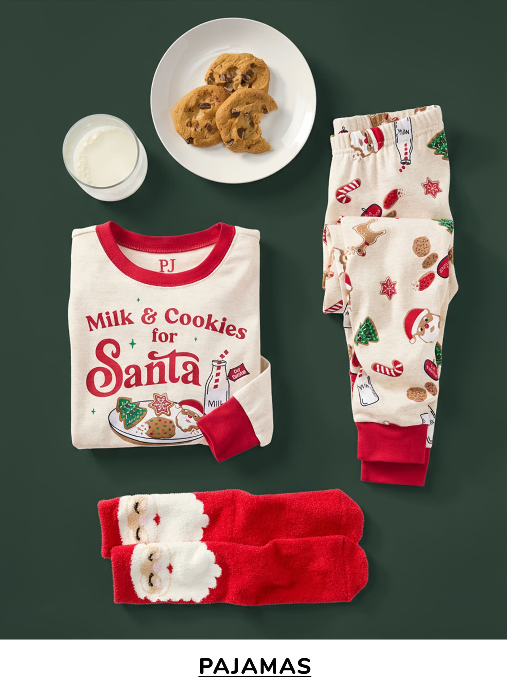 A plate of cookies, a "Milk & Cookies for Santa" t-shirt, and festive pajamas are arranged on a dark green background, creating a cozy and holiday-themed scene.