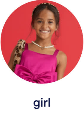 A young girl with a bright smile is wearing a pink dress and a floral headband against a solid red background.