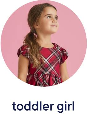 A young girl with long brown hair wearing a red plaid dress stands against a pink background, looking up with a thoughtful expression.