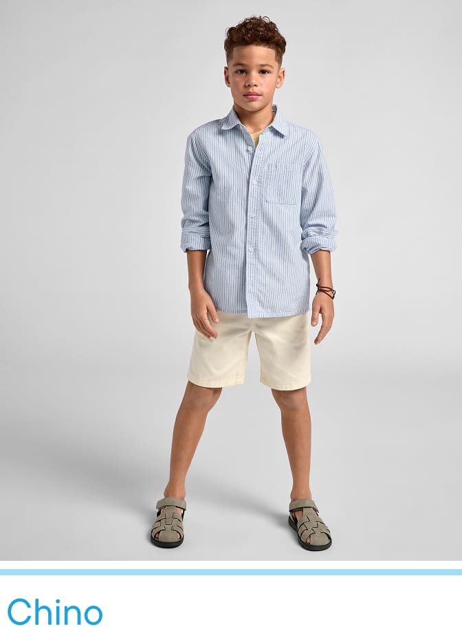 A young boy wearing a striped shirt and beige shorts stands against a plain white background, looking directly at the camera with a friendly expression.