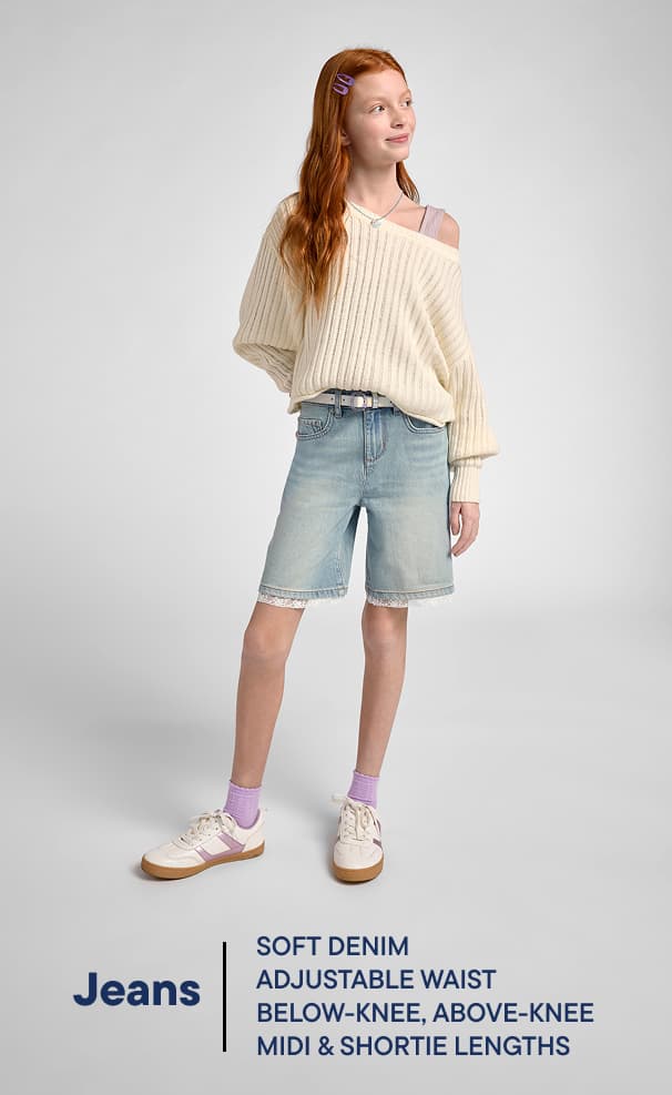 La imagen muestra a una joven que lleva un suéter color crema y pantalones cortos de mezclilla de color claro, de pie sobre un fondo liso.