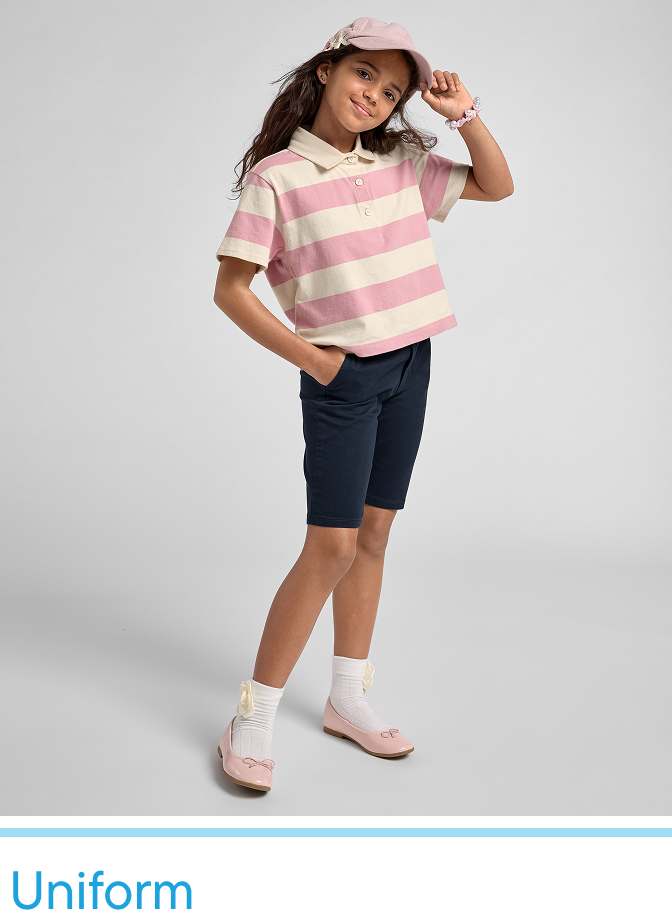 Una niña que viste una camisa a rayas rosas y blancas, pantalones cortos azul marino y sandalias blancas aparece sobre un fondo blanco liso.