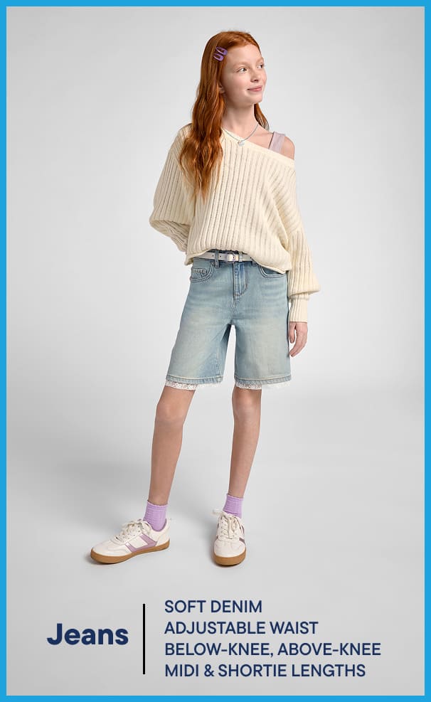 The image depicts a young woman wearing a cream-colored sweater and light-colored denim shorts, standing against a plain background.