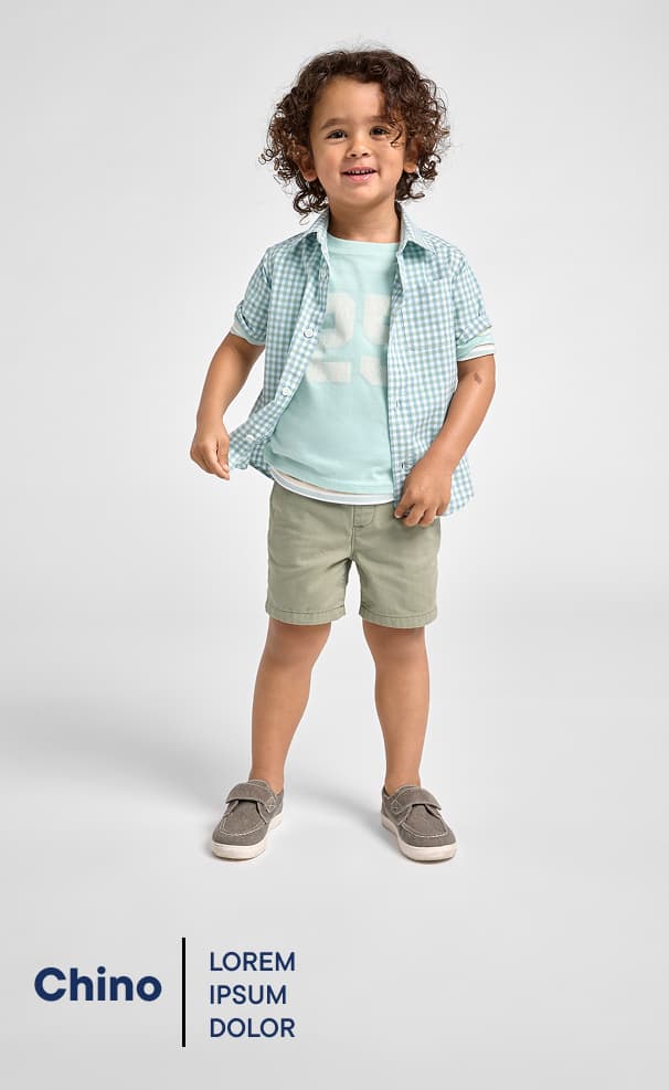 Una niña pequeña con cabello rizado, vestida con ropa de color claro, sonríe sobre un fondo blanco liso.