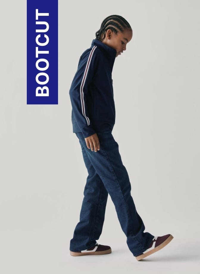 Una persona que viste un chándal azul marino con rayas blancas se encuentra delante de un gran logotipo "Bootcut" azul.