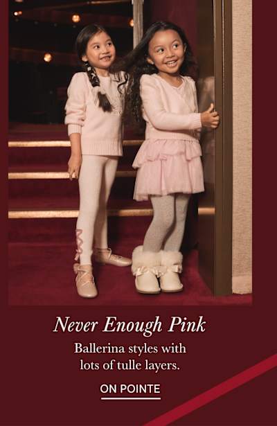 The image shows two young girls dressed in pink ballerina-style outfits, standing on a red-carpeted stage with a backdrop of lights and curtains.