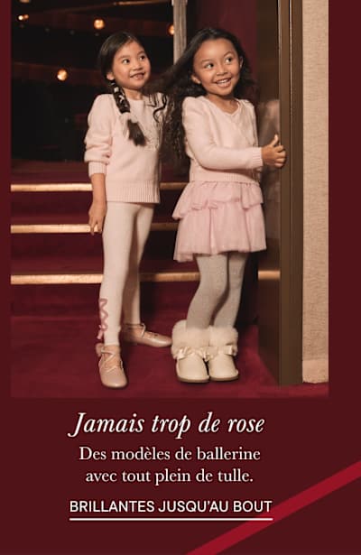 L'image montre deux jeunes filles vêtues de tenues roses de style ballerine, debout sur une scène recouverte d'un tapis rouge, avec en arrière-plan des lumières et des rideaux.