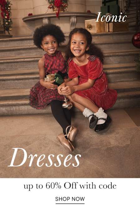 The image shows two young women wearing vibrant red dresses, posing together on a set of stairs with a sign advertising "Iconic Dresses" in the background.