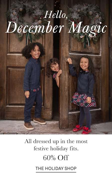 The image shows three young women dressed in festive holiday attire, standing in front of a wooden door decorated with holiday garlands and a sign that reads "Hello, December Magic".