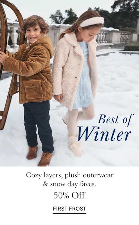 Two young women in warm winter coats standing in front of a snowy outdoor scene with a decorative archway in the background.