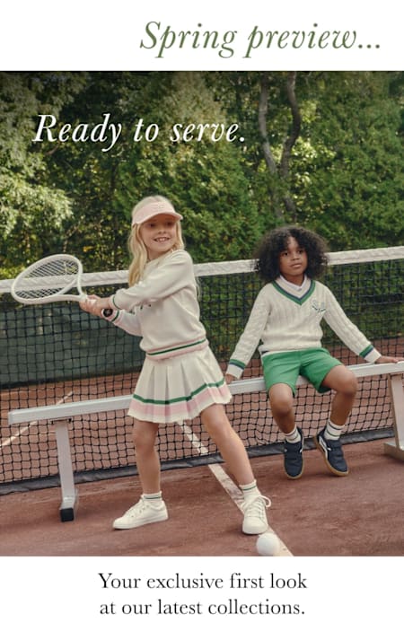Two young women in tennis attire standing on a tennis court, surrounded by lush greenery.