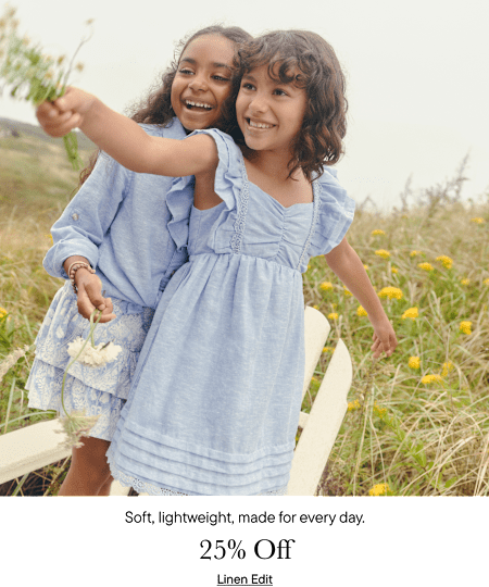 Two young girls in blue dresses are embracing and smiling in a field of flowers.