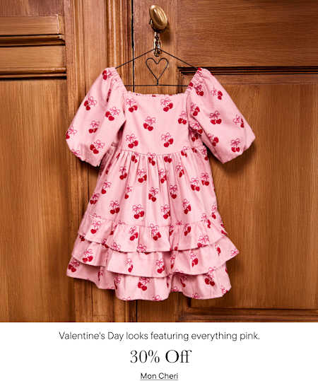 A pink, floral-patterned dress with puff sleeves and ruffled layers hangs on a metal hanger against a wooden background.