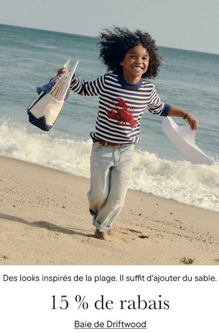 Une jeune personne aux cheveux bouclés court joyeusement sur une plage avec l'océan en arrière-plan, vêtue d'une chemise à rayures et portant un sac.