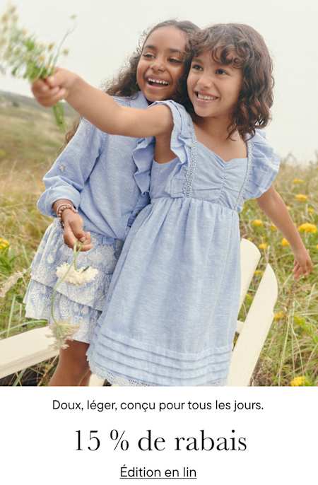 Deux jeunes filles en robes bleues sourient et s'enlacent dans un champ herbeux avec des arbres en arrière-plan.