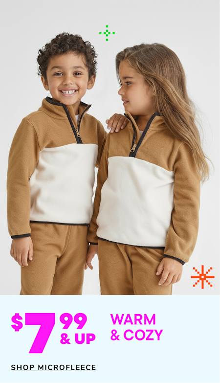 Two young children, a boy and a girl, are wearing matching beige hooded sweatshirts and smiling at each other in a warm and cozy setting.