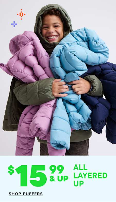 A smiling person wearing a hooded jacket is surrounded by various colorful puffy jackets displayed for sale.