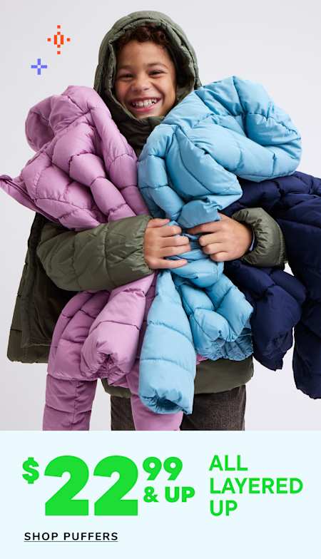 A smiling person wearing a hooded jacket is surrounded by various colorful puffy jackets displayed for sale.
