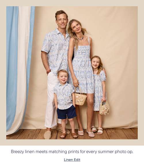 A family of four, dressed in matching light blue patterned outfits, poses in front of a neutral backdrop with draped fabric accents.