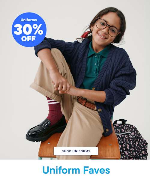 A smiling young woman wearing glasses and a navy blue sweater sits on a wooden stool, with a 30% off uniform sale sign in the background.