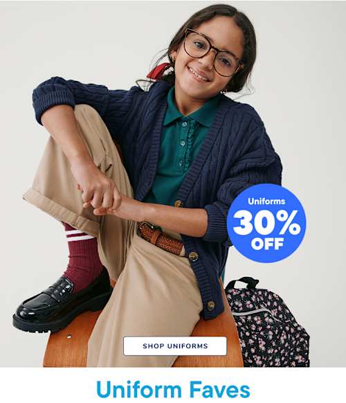 A smiling young woman wearing glasses and a navy blue sweater sits on a wooden stool, with a 30% off uniform sale sign in the background.