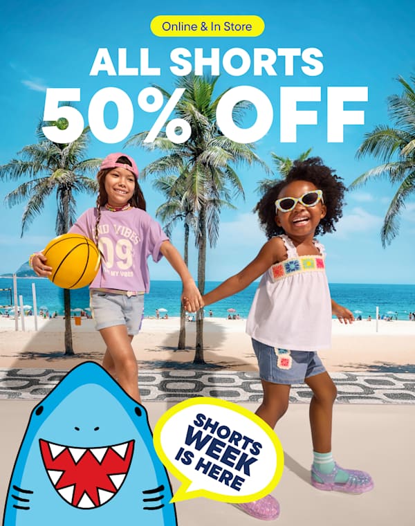 The image features two young girls standing on a beach with palm trees in the background, promoting a sale on all shorts with a 50% discount.