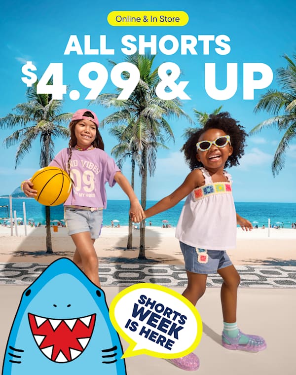 The image features two young girls standing on a beach with palm trees in the background, promoting a sale on all shorts with a 50% discount.