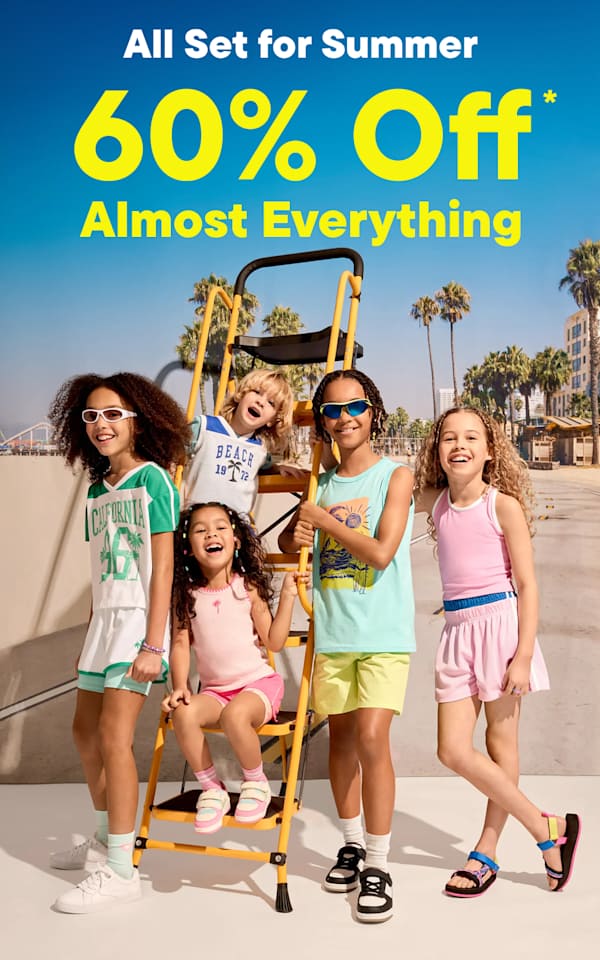 Five children in summer clothes stand on a beach boardwalk with a 60% off sale advertisement in the foreground and a pier and buildings in the background.