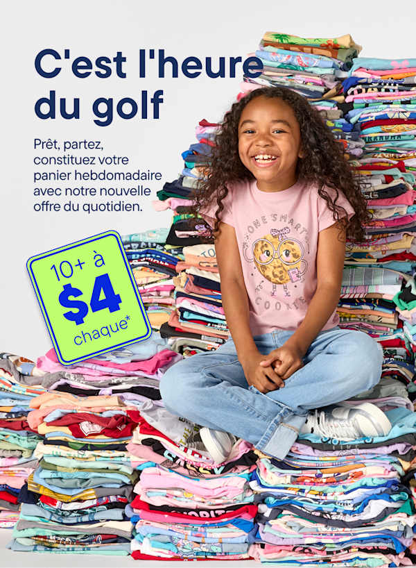 Une jeune fille souriante est assise en tailleur devant un énorme tas de t-shirts colorés, avec une pancarte verte annonçant une promotion au premier plan.
