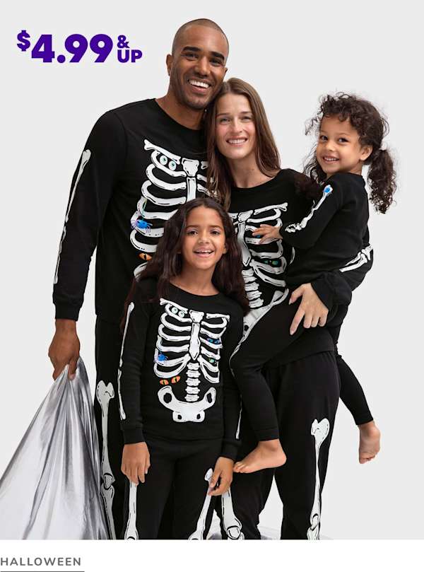 A happy family of four, dressed in matching skeleton-themed Halloween costumes, posing together against a plain white background.