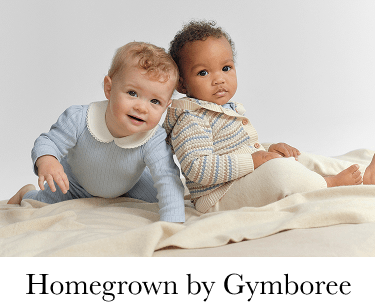 The image shows two young children, a boy and a girl, sitting on a soft, light-colored surface, with a plain background behind them.